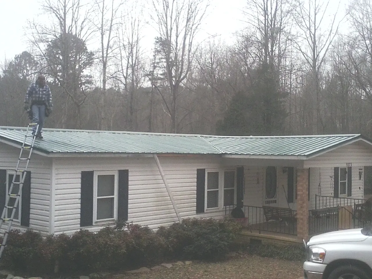 Worker on a ladder beside a new green metal roof on a ranch home in Susan