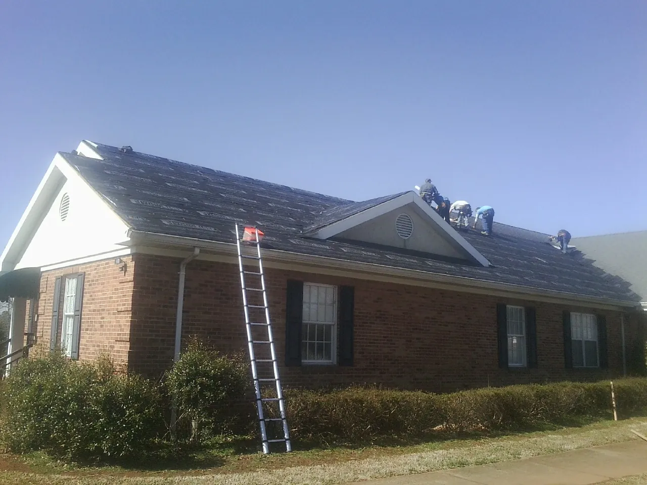 Crew tearing shingles off a brick ranch roof with a ladder set — Emergency Roof Repair work by our crew in Susan