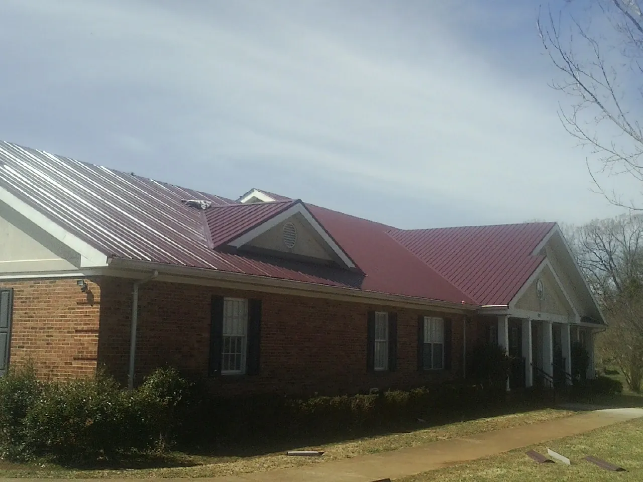 Red metal roof with gabled entries on a long brick building, from a Hail Damage Roof Repair job in Susan