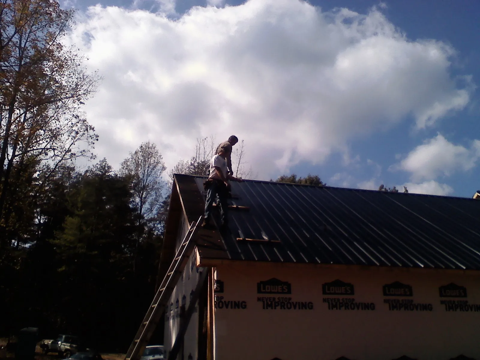 Roofer fastening dark metal panels high against a cloudy sky, from a Roof Inspection job in Susan