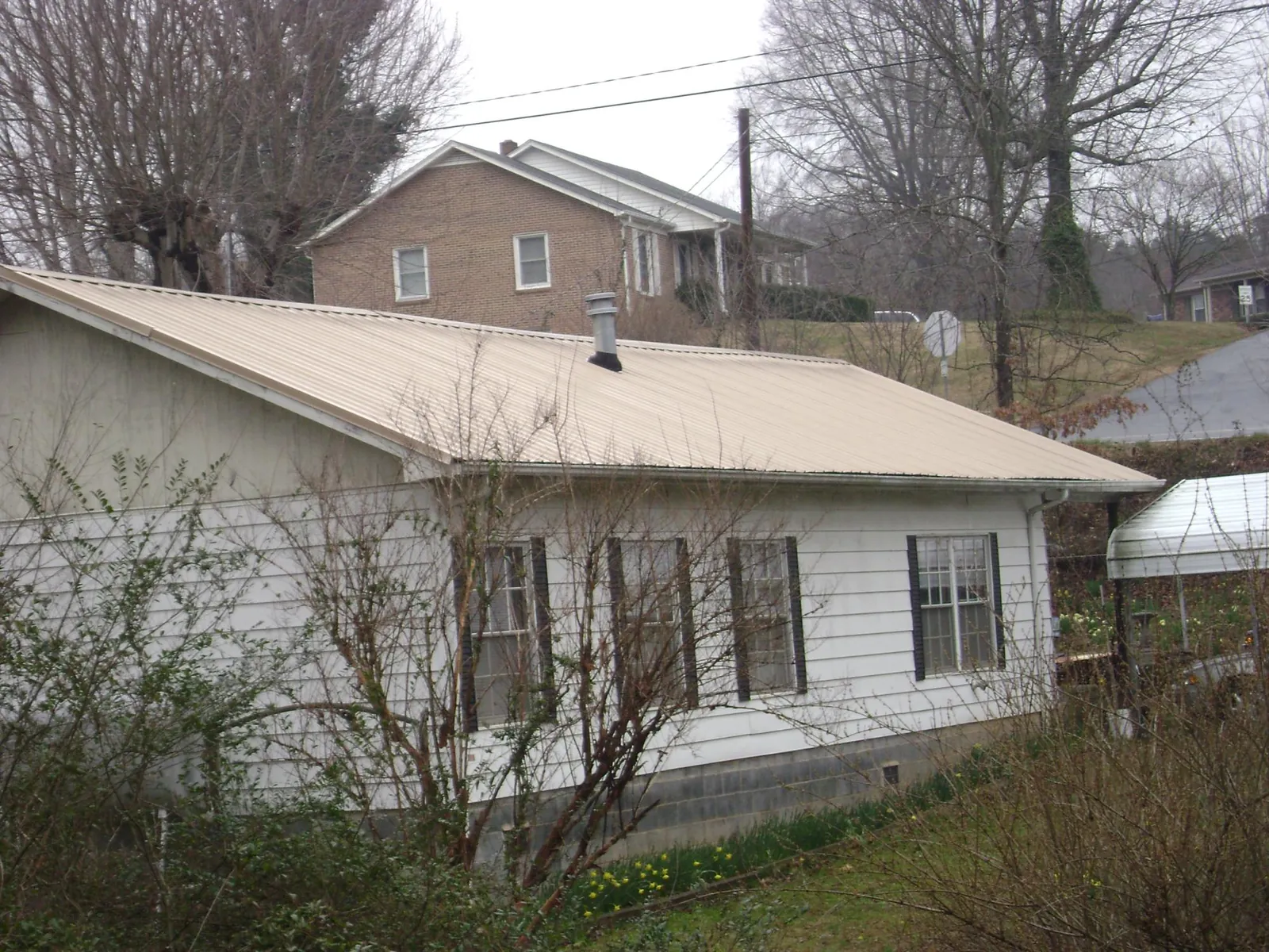 Tan metal roof on a white sided house set into a hillside — Commercial Roofing by Roofing Brothers in Susan