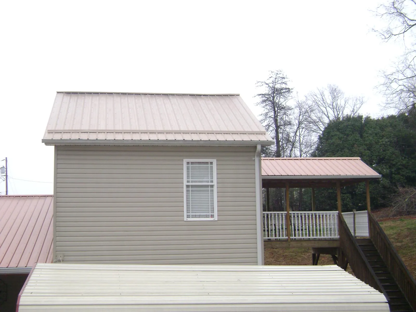 Tan metal roofs on a two story addition and attached porch, from a Roof Replacement job in Susan